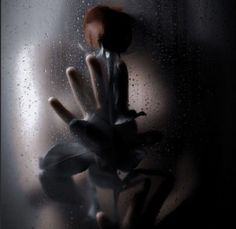 a hand reaching out through a window with rain drops