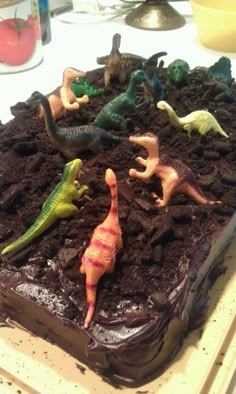 a cake with chocolate frosting and toy dinosaurs on top, sitting on a table