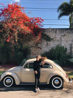 a woman standing next to an old car in front of a red flowered tree