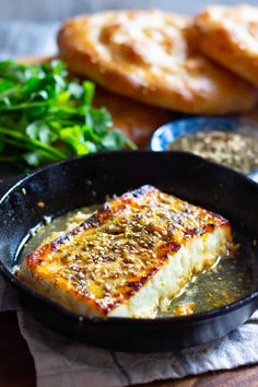 some food is in a black pan on a wooden table next to bread and greens