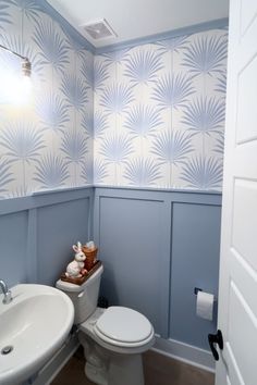 a white toilet sitting next to a sink in a bathroom under a window with palm leaves on the wall