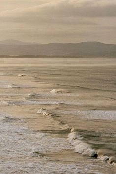 two surfers are riding the waves in the ocean on a cloudy day with mountains in the distance