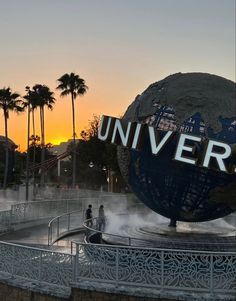 a large globe with the word universal on it in front of palm trees