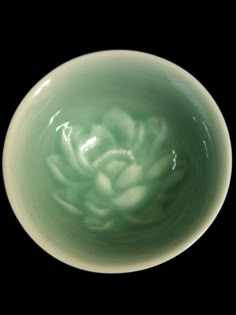 a green bowl with white flowers in it on a black background, showing the inside of the bowl