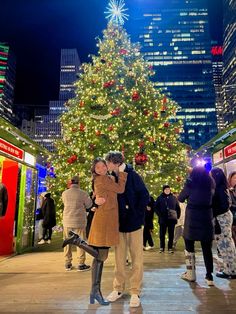 a man and woman kissing in front of a large christmas tree at the city center