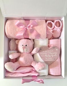 a pink teddy bear and baby clothes in a box with a heart on the inside