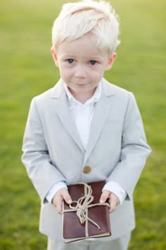 a little boy dressed in a suit and tie holding a brown box with a knot on it