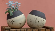 two vases with plants painted on them sitting on a wooden table next to a pink wall