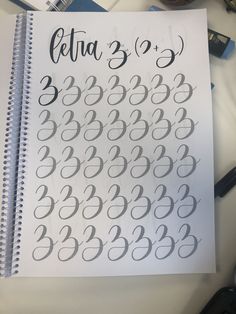 a spiral notebook with the numbers written in cursive writing on it and some pens next to it