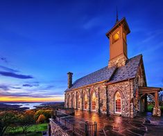 an old stone church with a clock tower on top is lit by the sun set