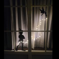 a silhouette of a person standing in front of a window with fairy lights on it