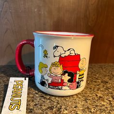 a red and white coffee mug sitting on top of a counter next to a sign