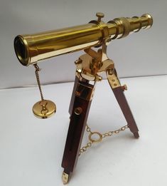 an antique brass plated telescope on a wooden tripod with chain attached to it