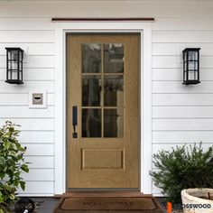 the front door to a white house with two lanterns on it