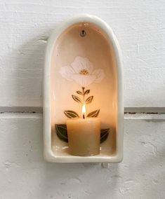 a candle that is sitting inside of a white wall mounted holder with flowers on it