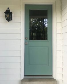 a green door on the side of a white house with a light blue front door