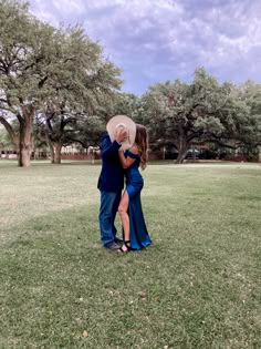 a man and woman standing in the grass with their arms around each other, embracing