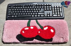 a computer keyboard sitting on top of a pink rug with two cherries attached to it