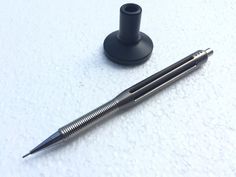 a pen sitting on top of a white table next to a black holder with a metal tip