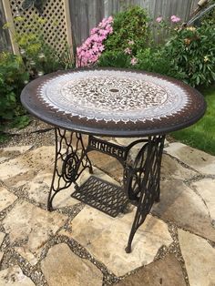 an old sewing machine table is sitting on a patio with pink flowers in the background