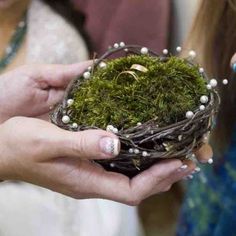 two women holding a moss covered bird's nest with pearls and leaves on it