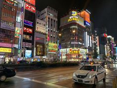 a busy city street at night with lots of neon signs on the buildings and cars