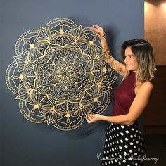 a woman standing next to a wall with a large gold flower design on it