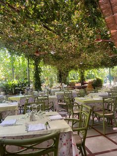 an outdoor dining area with tables and chairs covered in greenery, surrounded by trees