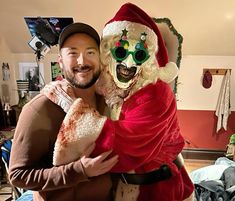 a man in a santa claus costume hugging a creepy looking person with green glasses on