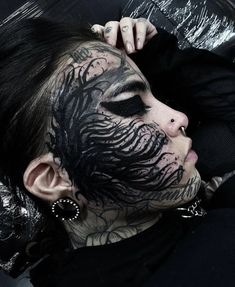 a woman with black face paint and tattoos on her face is posing for the camera