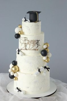 a three tiered white cake with black and gold decorations on the top, topped with a graduation cap