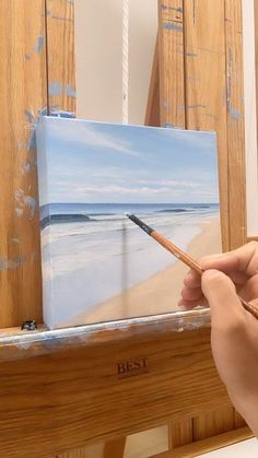 a person holding a paintbrush in front of an easel with a painting on it