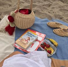 a person laying on the beach with some fruit and books in front of them,