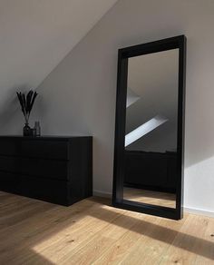 a large mirror sitting on top of a wooden floor next to a dresser and vase