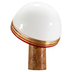 a white and gold table lamp sitting on top of a wooden base with a red stripe around it