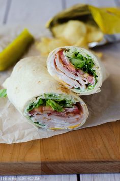 two wraps with meat, lettuce and cheese on a cutting board next to pickles