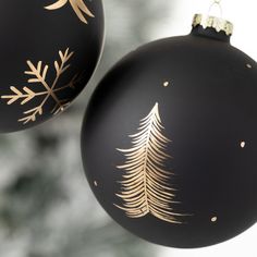 two black and gold christmas ornaments hanging from a tree with snowflakes on them