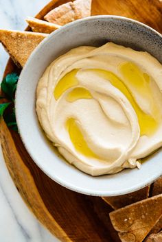 a white bowl filled with hummus and tortilla chips on top of a wooden platter