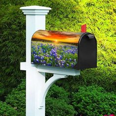 a mailbox with blue flowers painted on it in front of some bushes and trees