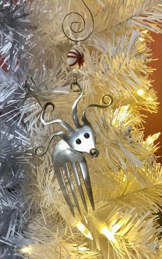 a christmas ornament hanging from the side of a white tree with silver tinsel