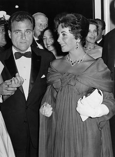 an old black and white photo of two people standing next to each other in formal attire