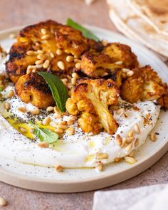 a white plate topped with cauliflower covered in yogurt and pine nuts