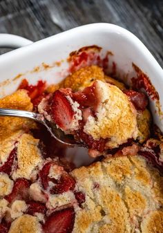 a spoonful of strawberry cobbler is being lifted from the casserole dish