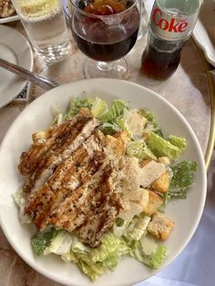 a white plate topped with salad and meat next to two glasses of coke on a table