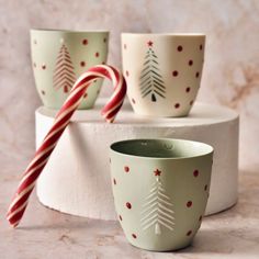 three mugs decorated with christmas trees and candy canes on a marble countertop