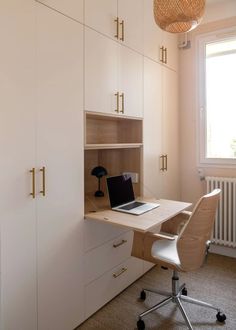 a desk with a laptop on it in front of some cupboards and a window