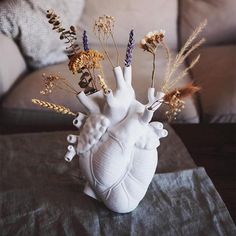 a heart shaped vase with dried flowers in it on a table next to a couch