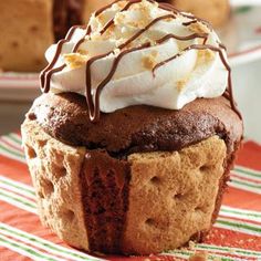 a cupcake with whipped cream and chocolate on top sitting on a striped table cloth