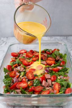 someone is pouring dressing into a salad in a glass dish with tomatoes and lettuce