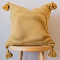 a yellow pillow with tassels sits on a wooden stool next to a white wall